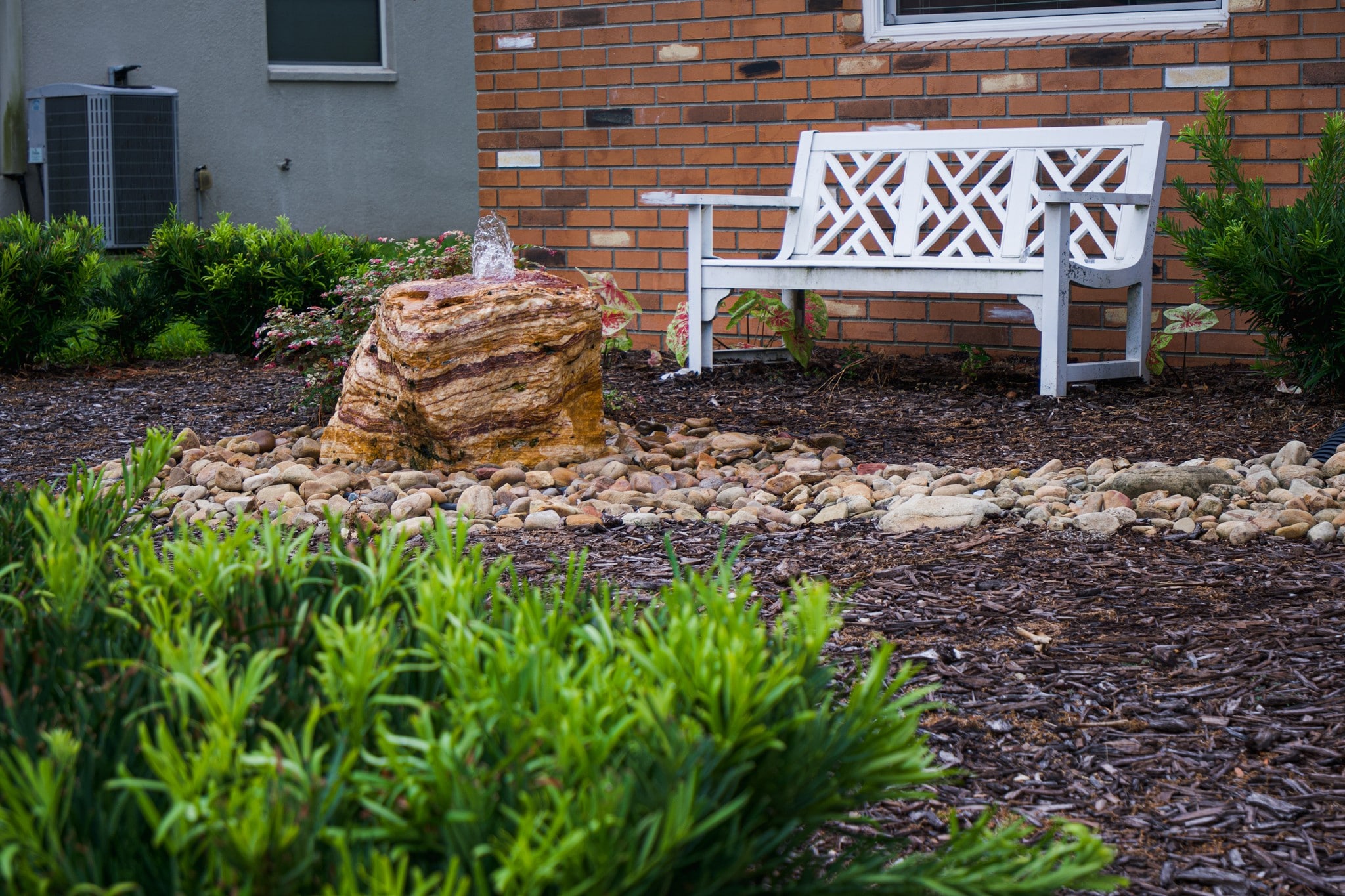 water fountain with natural rock, white bench and mulched garden bed