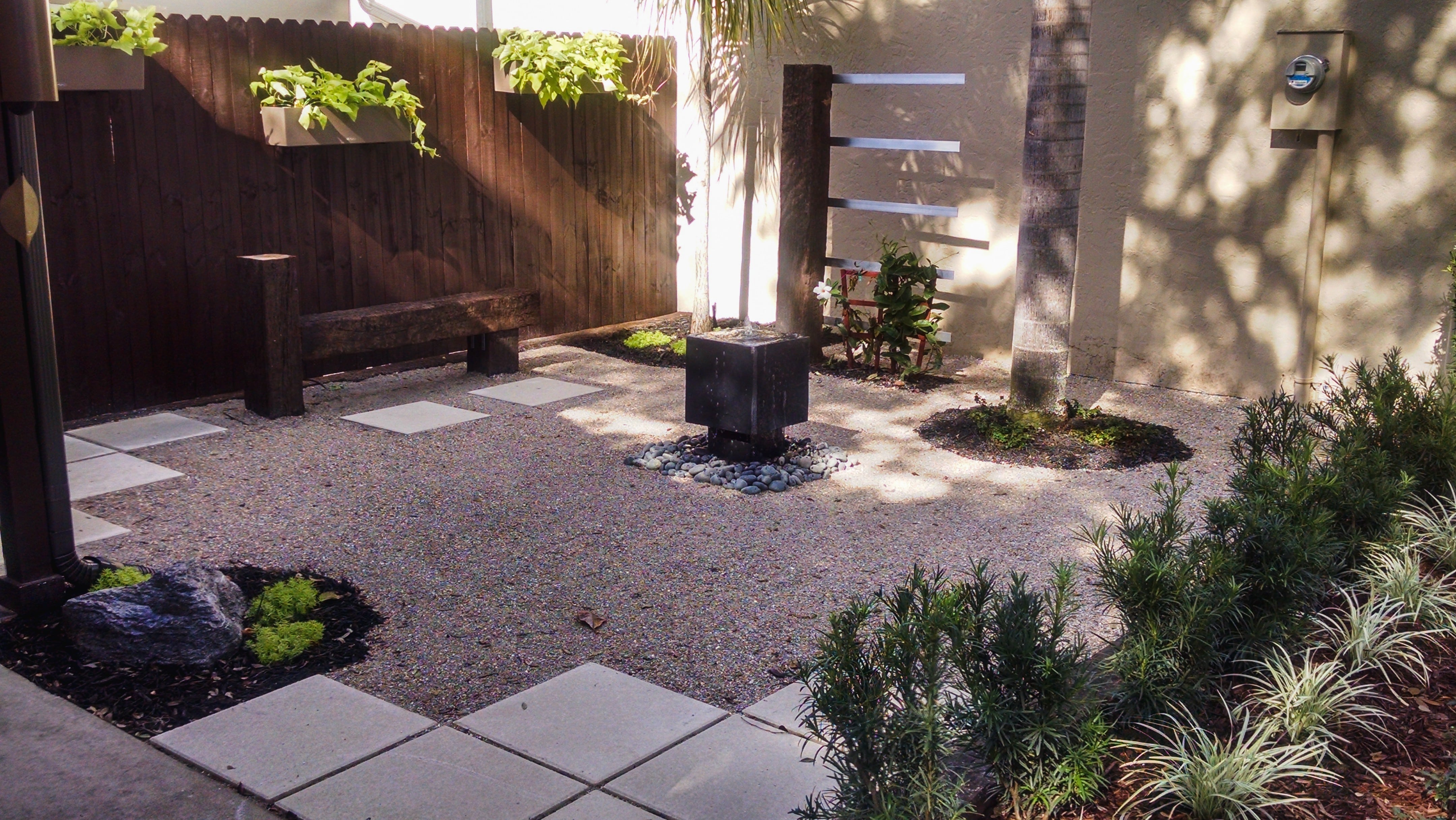 meditative minimalist rock garden with water fountain, hanging planter boxes and flower beds
