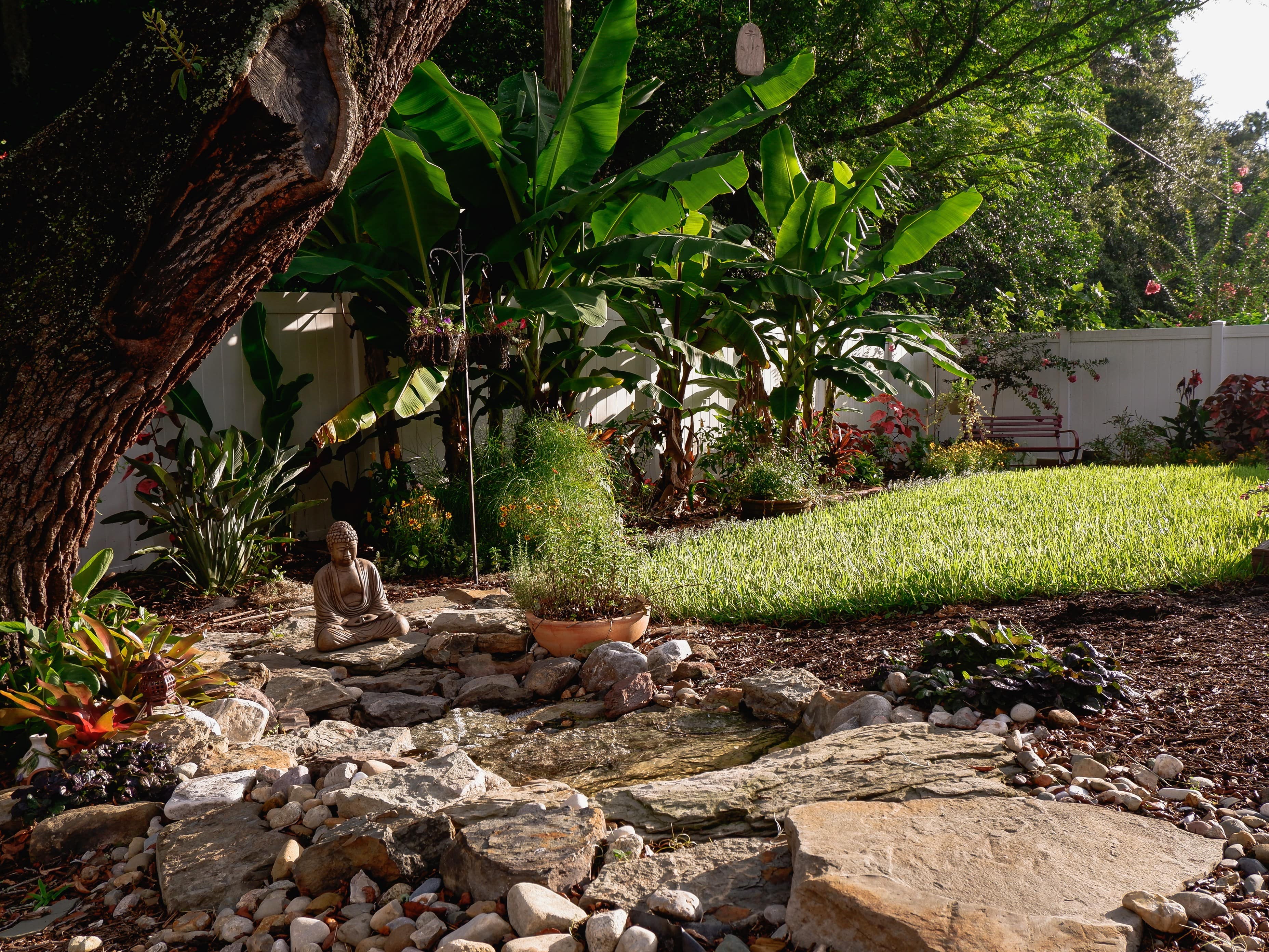 backyard landscaping with waterfall, statue, natural rock landscape and colorful plant garden
